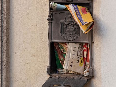 Überquellender metallener Briefkasten an einer Hauswand, Prospekte ragen heraus