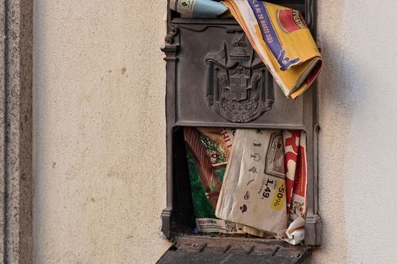 Überquellender metallener Briefkasten an einer Hauswand, Prospekte ragen heraus