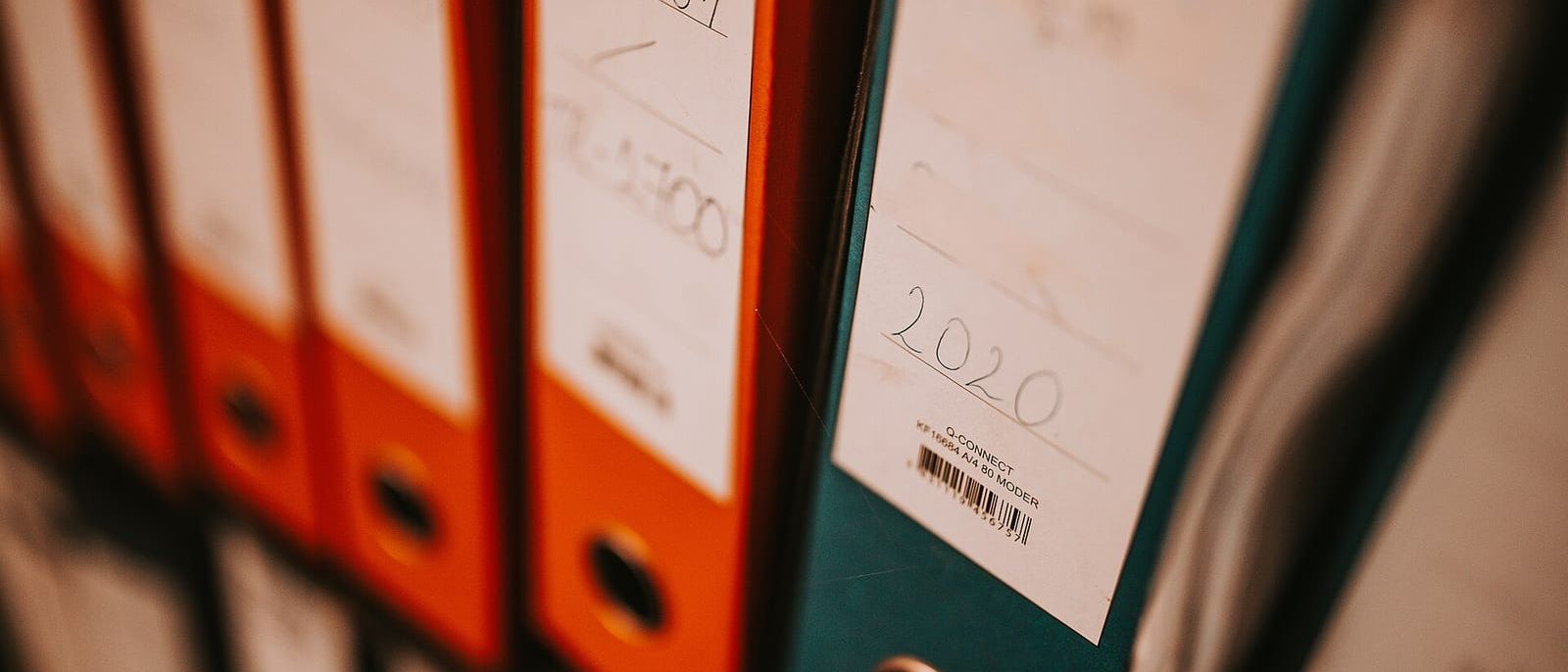 Aktenordner in Orange und Petrol im Regal, Rückenschild mit Jahreszahl 2020