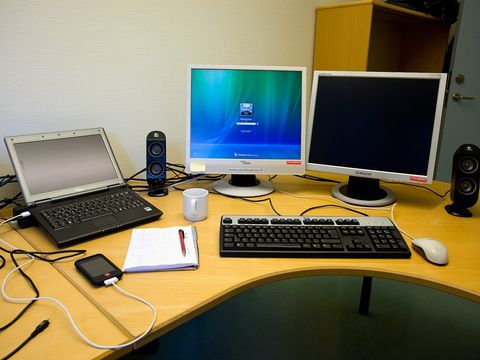 Büroschreibtisch mit Laptop, zwei Monitoren, Tastatur, Notizblock und Kaffeetasse