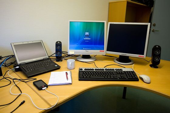Büroschreibtisch mit Laptop, zwei Monitoren, Tastatur, Notizblock und Kaffeetasse