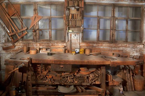 Alte Schreinerwerkstatt mit Hobelbank, Holzresten und Werkzeug vor Sprossenfenstern