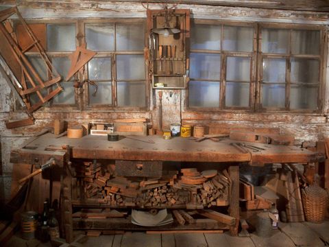 Alte Schreinerwerkstatt mit Hobelbank, Holzresten und Werkzeug vor Sprossenfenstern